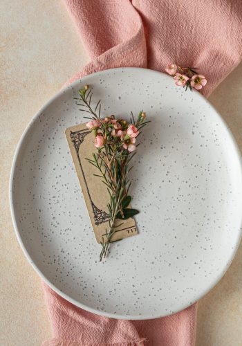 Romantic, wedding or spring table setting. Empty plate with card and little pink flowers, light concrete background. Flat lay. Selective focus.